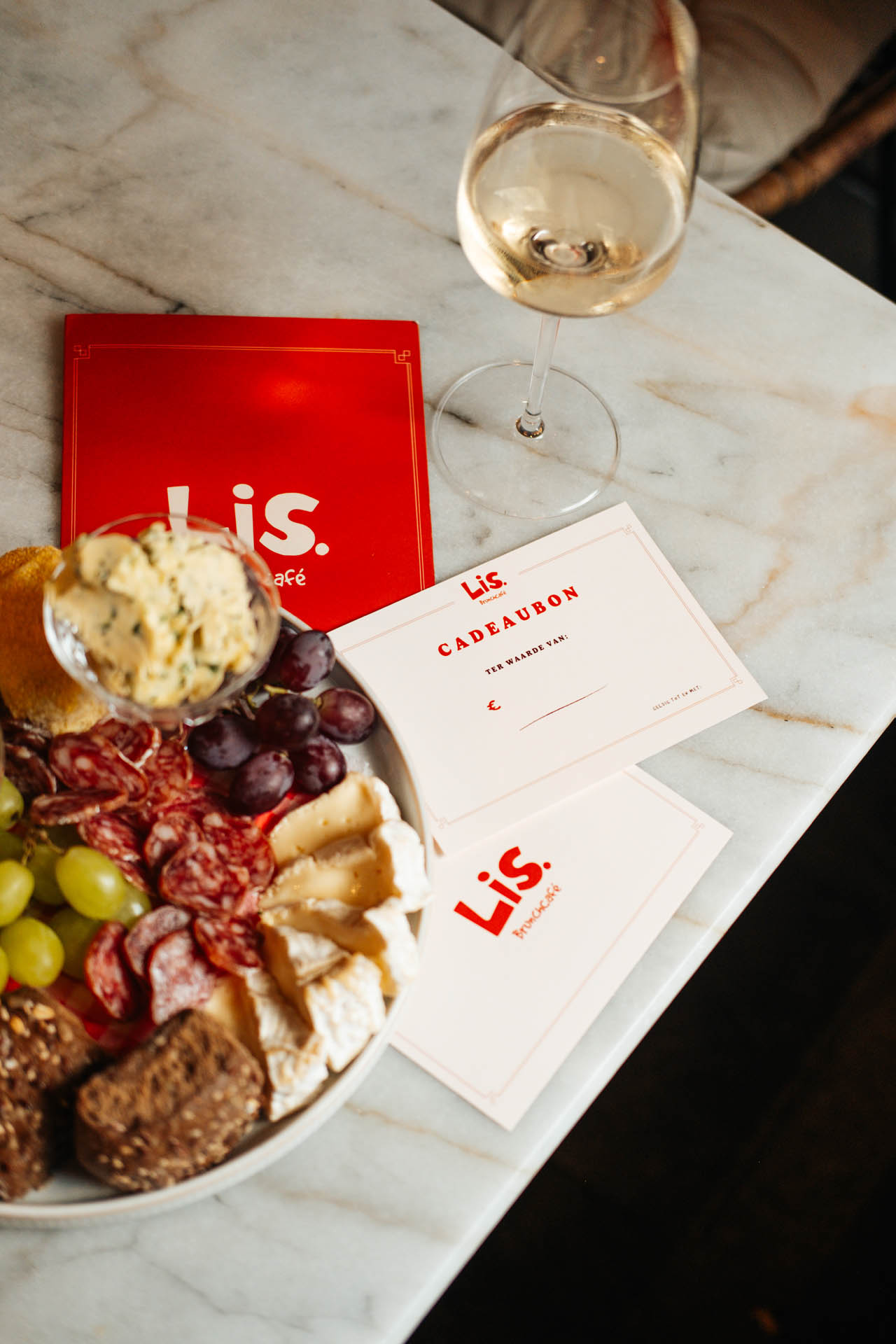 Charcuterieplank met wijn en cadeaubonnen op marmerentafel.